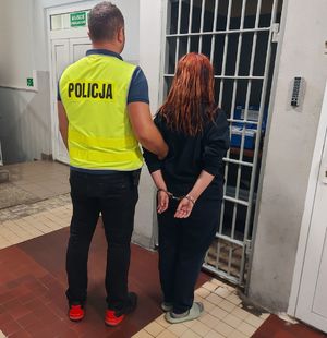 policjant z zatrzymaną kobietą zakutą w kajdanki stoi przed kratami
