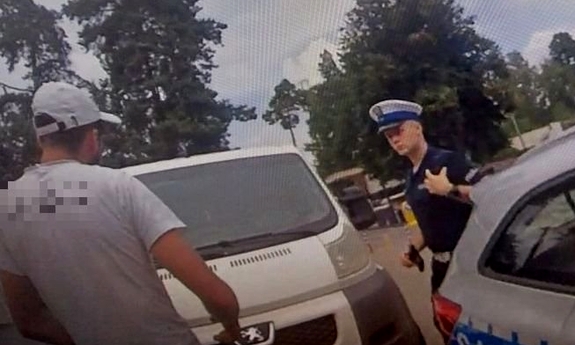 screen z kamery nasobnej przedstawia policjanta rozmawiającego z mężczyzną przy samochodzie i radiowozie