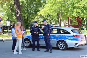 przy radiowozie stoi dwóch umundurowanych policjantów, obok stoją trzy kobiety w kamizelkach odblaskowych