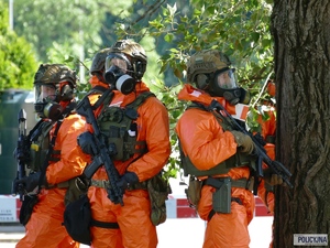 policjanci w specjalnych pomarańczowych strojach stoją za drzewem