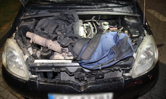 torby leżące na silniku pod podniesioną maską samochodu, obok widoczny katalizator