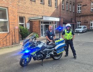 Na zdjęciu dwóch policjantów stojących przy motocyklu służbowym przed budynkiem szpitala