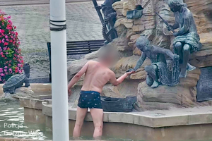 Stopklatka z monitoringu miejskiego przedstawia mężczyznę, który stoi w fontannie i dotyka ręki figurki
