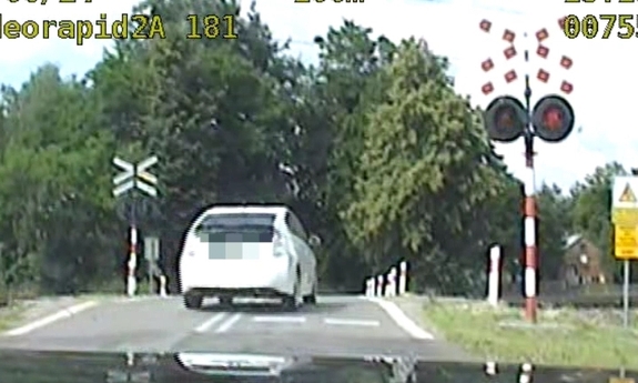 Stopklatka z nagrania wideorejestratora przedstawia samochód w kolorze białym wjeżdżający na przejazd kolejowy