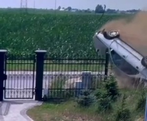widoczny koziołkujący samochód na jezdni przed ogrodzeniem posesji