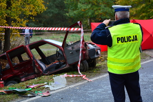 policjant ruchu drogowego robi telefonem zdjęcie rozbitego pojazdu
