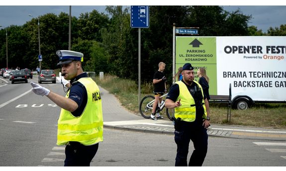 policjant ruchu drogowego kieruje ruchem drogowym, za nim widoczny jest innym umundurowany policjant, a z tyłu plakat promujący Open&#039;er Festival