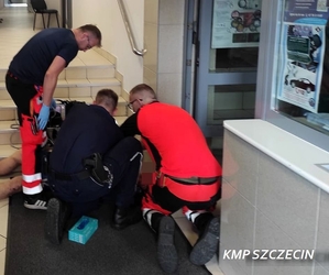 policjant i dwaj ratownicy medyczni przy mężczyźnie leżącym przy schodach na korytarzu w budynku
