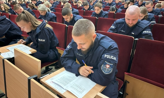 funkcjonariusze siedzą na sali w fotelach pisząc egzamin