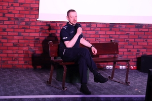 Komendant Główny Policji przemawia do zgromadzonych na widowni gości siedząc na ławce ustawionej na scenie