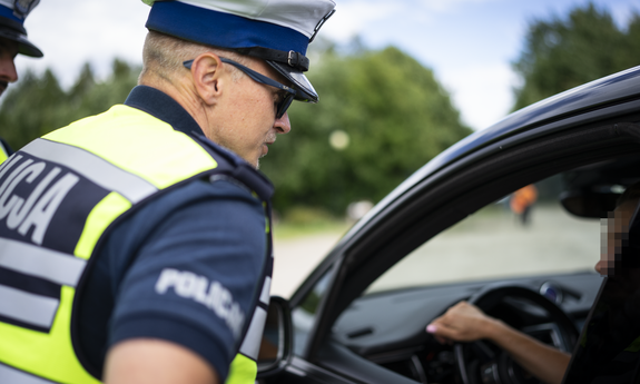 policjant ruchu drogowego podczas kontroli drogowej rozmawia z kierowcą siedzącym w samochodzie