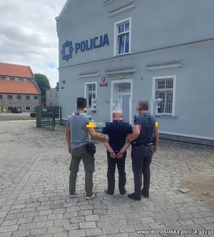 policjanci stoją z zatrzymanym przed budynkiem policji