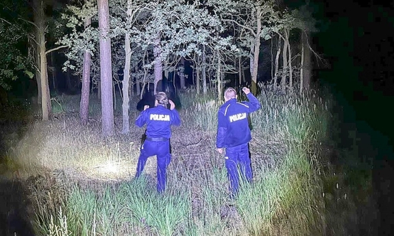 pora nocna. Dwaj funkcjonariusze w lesie z latarkami podczas poszukiwań zaginionej osoby