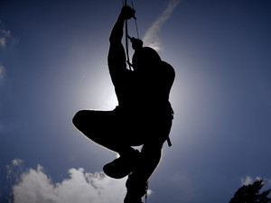 Ciemna sylwetka mężczyzny wspinającego się po drabince sznurowej na tle jasnego nieba.