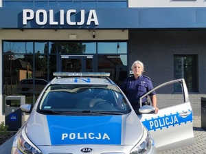 policjantka stoi przy radiowozie, w tle budynek komisariatu Policji