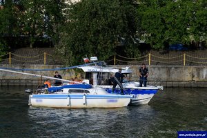 Policyjna łódka, a na niej policjanci, obok niej żaglówka