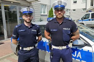 dwóch umundurowanych policjantów stoi przy radiowozie