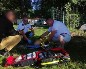 Policjant i ratownik pomagają 16-latce, która leży na trawie owinięta kocem ratunkowym
