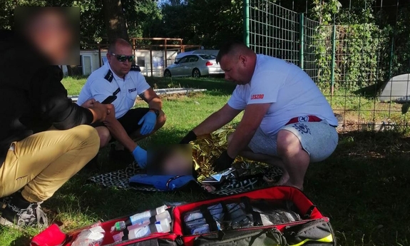 Policjant i ratownik pomagają 16-latce, która leży na trawie owinięta kocem ratunkowym