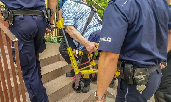 policjanci znoszą osobę na wózku inwalidzkim