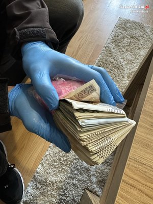 plik banknotów trzymany w dłoniach, na których są założone gumowe niebieskie rękawiczki