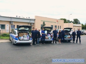 policjanci stoją przy otwartych bagażnikach radiowozów pełnych jedzenia dla zwierząt