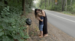 kadr z filmu: kobieta i małe dziecko stoją przy przydrożnym krzyżu
