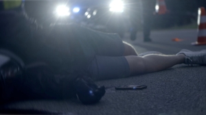 kadr z filmu: osoba leży na drodze po wypadku drogowym