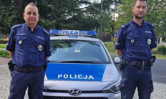na zdjęciu dwóch umundurowanych policjantów stoi przy radiowozie