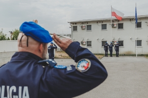 Salutujący funkcjonariusze naprzeciwko masztu z polską flagą