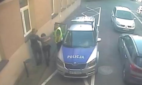 Policjanci wraz z zatrzymanym mężczyzną przy zaparkowanym na ulicy radiowozie