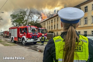 na zdjęciu policjantka zabezpieczająca miejsce zdarzenia podczas akcji gaśniczej strażaków