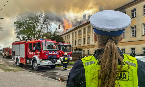 Policjantka zabezpieczająca miejsce zdarzenia podczas akcji gaśniczej strażaków