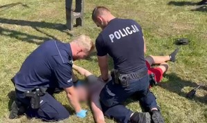 dwaj policjanci reanimują mężczyznę leżącego na ziemi obok słupa energetycznego