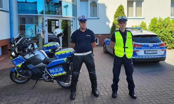 dwaj policjanci stoją przed budynkiem komendy Policji, za nimi stoją dwa motocykle i radiowóz