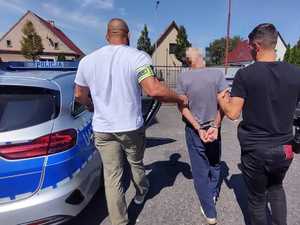 dwóch policjantów prowadzi zatrzymanego mężczyznę do radiowozu