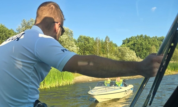 funkcjonariusz na łodzi policyjnej, obok niej łódź motorowa z awarią silnika