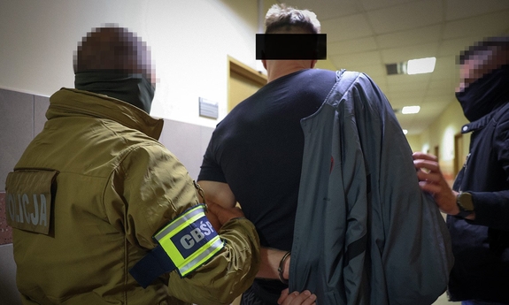 dwaj funkcjonariusze  z zatrzymanym zakutym w kajdanki