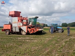 kombajn oraz ciągnik rolniczy stoją na polu, nad nimi są linie energetyczne