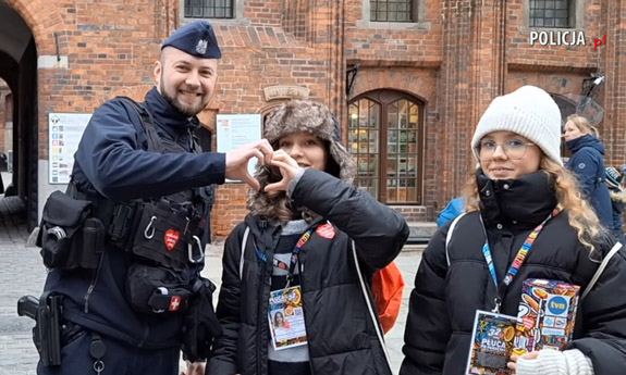 Policjant i dwie wolontariuszki WOŚP, policjant i wolontariuszka układają dłonie w kształt serca.