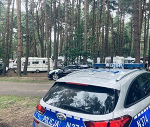 pojazdy na campingu wśród drzew, na pierwszym planie radiowóz policyjny