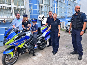 chłopiec na motocyklu policyjnym, obok stoją policjanci