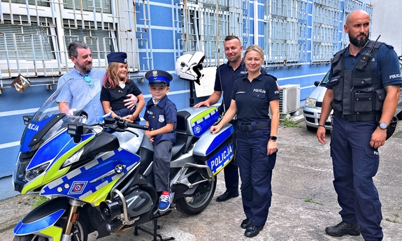 chłopiec na motocyklu policyjnym, obok stoją policjanci