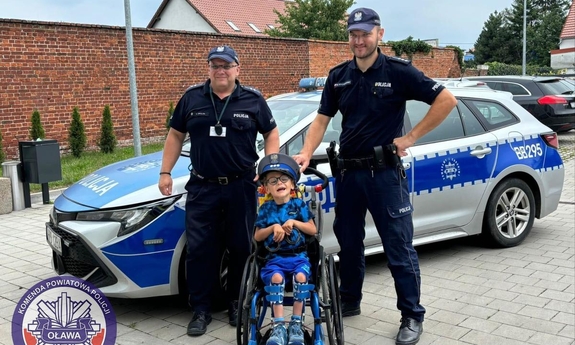Dwaj policjanci pozują do zdjęcia wraz z chłopcem siedzącym na wózku inwalidzkim