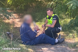 na zdjęciu umundurowany policjant klęka przy odnalezionym mężczyźnie, senior pije wodę, w tle las