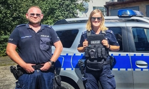 policjant i policjantka stoją przed radiowozem