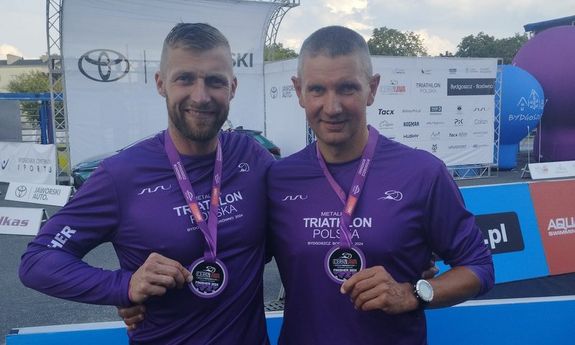 dwóch mężczyzn pozuje do zdjęcia z medalami