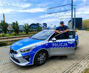 na zdjęciu umundurowany policjant stoi przy radiowozie