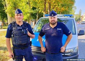 na zdjęciu umundurowani policjanci stoją na tle radiowozu