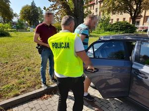 dwóch policjantów prowadzi zatrzymanego mężczyznę do radiowozu